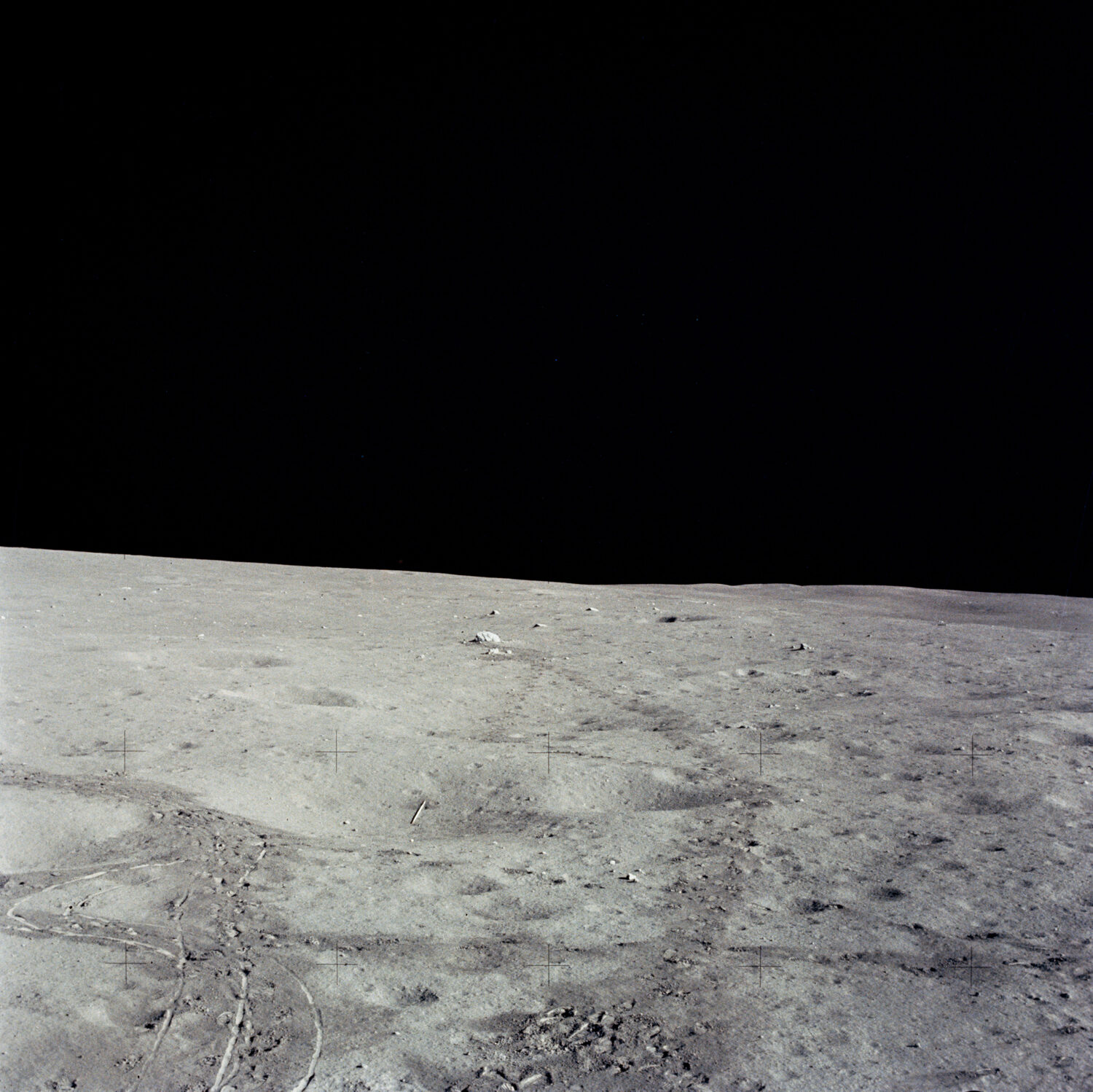 A NASA photograph of the lunar surface showing the small white golf ball and the javelin left by Alan Shepard during Apollo 14, with bootprints and tracks in the gray regolith.