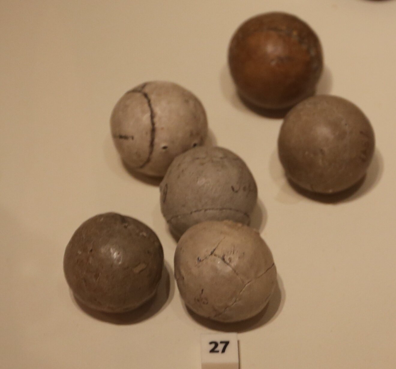 A collection of antique featherie golf balls, hand-stitched leather spheres stuffed with feathers, showing visible seams and age, on display in a museum.